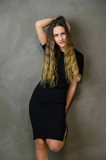 Vertical photo style girl with beautiful long hair in a black dress on a gray background in the studio - Foto, afbeelding