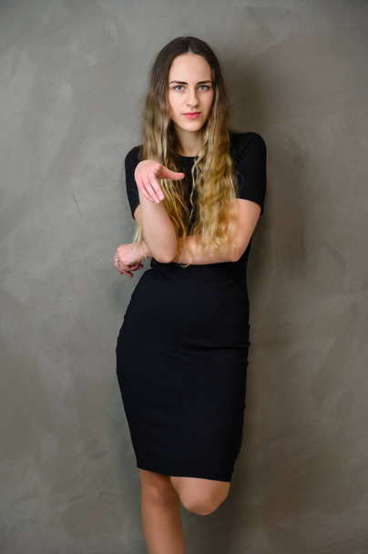 Vertical photo style girl with beautiful long hair in a black dress on a gray background in the studio - Photo, Image