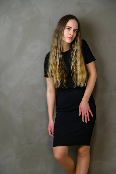 Vertical photo style girl with beautiful long hair in a black dress on a gray background in the studio - Φωτογραφία, εικόνα