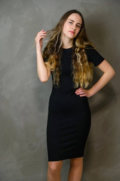 Vertical photo style girl with beautiful long hair in a black dress on a gray background in the studio - 写真・画像