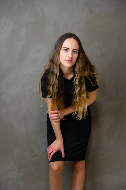 Vertical photo style girl with beautiful long hair in a black dress on a gray background in the studio - Valokuva, kuva