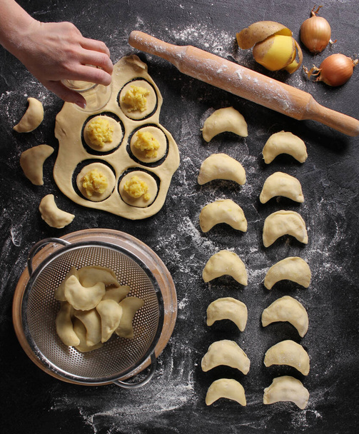 Concept of Ukrainian cuisine. Dumplings with potatoes on a dark background with hands. Cooking process - Φωτογραφία, εικόνα