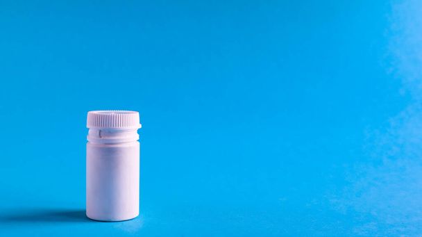White pills and white plastic little bottle with copy space on dark blue background, concept of health and medicine. Copy space for your text. Healthcare concept. Medical social media blog template - 写真・画像