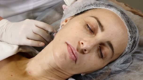 Eldivenli kozmetik uzmanı boyun kaldırma iğnesi yapıyor. Kadın müşteri sağlık kliniğinde yüz güzelliği ameliyatı oluyor. Kırışıklık önleyici kolajen ve hiyalüronik asit enjeksiyonları. Tam Hd - Video, Çekim