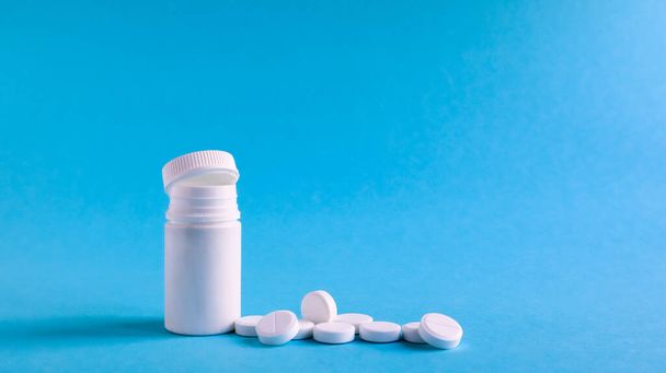 White pills and white plastic little bottle with copy space on dark blue background, concept of health and medicine. Copy space for your text. Healthcare concept. Medical social media blog template - Photo, Image