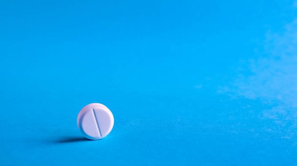 White round medical pills on a blue background. Scattered white pills on the table. The concept of medicine, pharmacy and healthcare. Copy space Empty space for text or logo - Foto, imagen