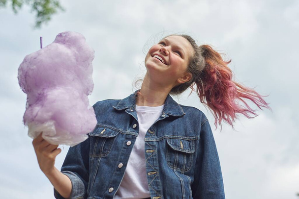 Beautiful smiling teenage girl with pink hair, hairstyle holding candy floss. Blue sky background, copy space - Zdjęcie, obraz