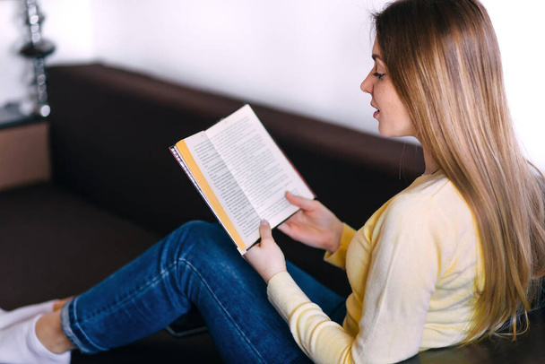 young woman sitting on sofa reading book - Photo, Image