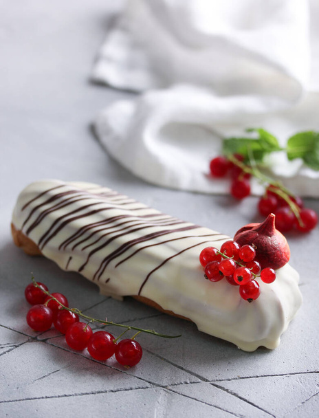 Dessert. Eclair with cream in white glaze with red berries. Sweet pastry tube with cream and red berries on a light background. Background image, copy space - Fotó, kép