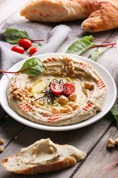 Oriental cuisine. Traditional snack hummus. It includes chickpeas, pine nuts, olive oil, spices and lemon juice. Herbs and tomatoes on a light wooden background.  - Photo, image