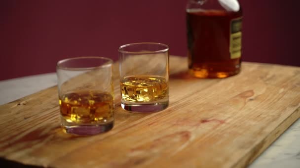 Bardaki ahşap tahtanın üzerinde kristal bardaklarda buz küpleri olan eski, lezzetli bir viski. Stres ve işten sonra rahatlamak için bir şişe viski. Kadim alkol içeceği. - Video, Çekim