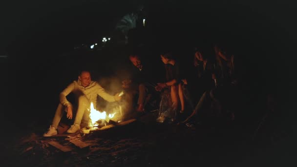 Bir grup arkadaş, gece deniz kenarındaki kumsalda kamp ateşinin yanında eğleniyor. Hızlı video, yavaş çekim, tam yol ileri. - Video, Çekim