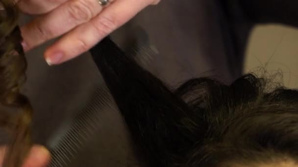 Stylistka hřebeny a narovnává kudrnaté vlasy brunetky dívka - Záběry, video