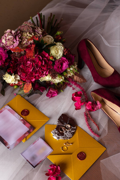 αξεσουάρ γάμου: μπουκέτο νύφων με τριαντάφυλλα, παιώνιες και ορτανσίες, βέρες σε πέτρα, δαχτυλίδι και σκουλαρίκια με διαμάντια, γυναικεία παπούτσια, πρόσκληση και κίτρινοι φάκελοι με κόκκινη κέρινη σφραγίδα - Φωτογραφία, εικόνα