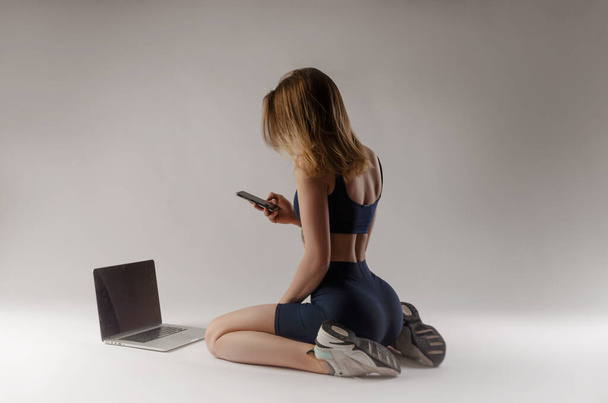 atletická dívka pózující ve studiu provádění cvičení on-line na notebooku na bílém pozadí - Fotografie, Obrázek