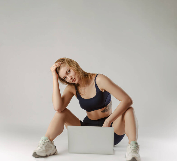 спортивна дівчина позує в студії, виконуючи вправи онлайн на ноутбуці на білому тлі
 - Фото, зображення