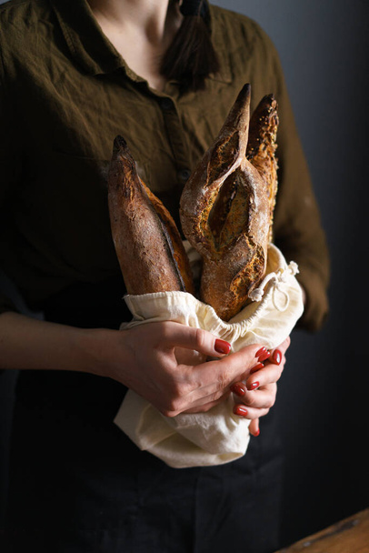 Valikoima ranskalaista leipää leipäpussissa naisten leipuri tilalla, patonkeja ja yrtti fougasse. pystyvalokuva
 - Valokuva, kuva