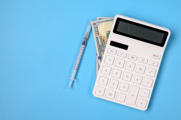 .Lugar de trabajo de un médico con una calculadora, dinero y una jeringa sobre un fondo azul con espacio vacío para el texto
. - Foto, imagen