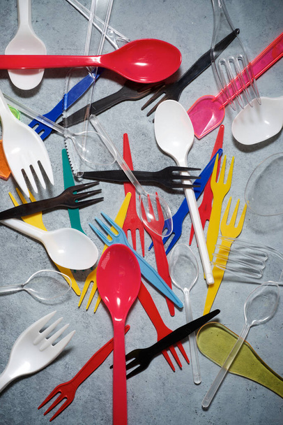 Πολύχρωμα πλαστικά μαχαιροπίρουνα σε ένα πέτρινο τραπέζι. - Φωτογραφία, εικόνα