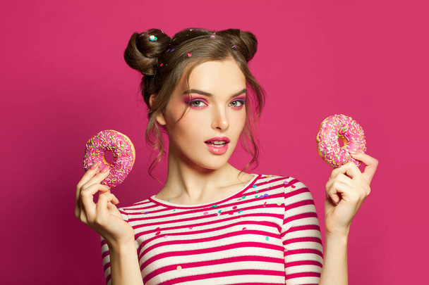 Aantrekkelijke vrouw tonen donuts op levendige roze achtergrond - Foto, afbeelding