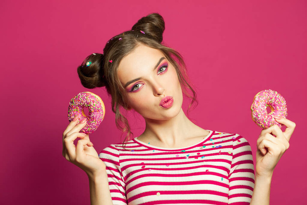 Cute woman holding donut on vivid pink background, diet concept - 写真・画像