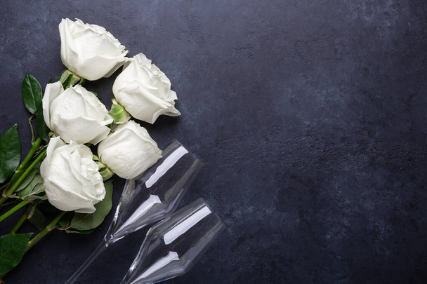 White rose flowers bouquet, champagne glasses on black stone background Romantic greeting card Copy space Top view - Foto, afbeelding