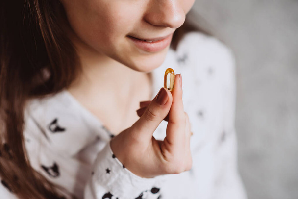 Diet. Nutrition. Smiling girl taking pills with oil Omega-3 cod liver and holding a glass of fresh water in the morning. The concept of a healthy eating and lifestyle. Vitamin D, E, Fish Oil Capsules. - Fotografie, Obrázek