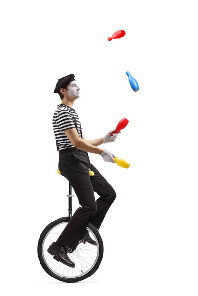 Full length profile shot of a pantomime guy riding a mono-cycle and juggling isolated on white background - Photo, Image