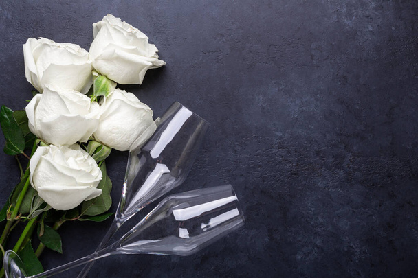 White rose flowers bouquet, champagne glasses on black stone background Romantic greeting card Copy space Top view - Photo, Image