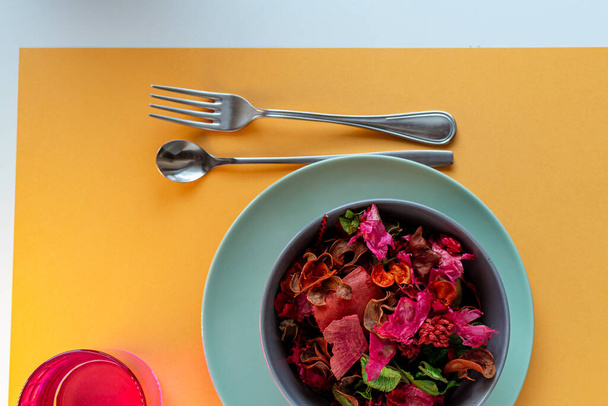 Μοντέρνα επιτραπέζια σκεύη με πιάτο, γυαλί και μαχαιροπήρουνα στο πολύχρωμο τραπέζι - Φωτογραφία, εικόνα