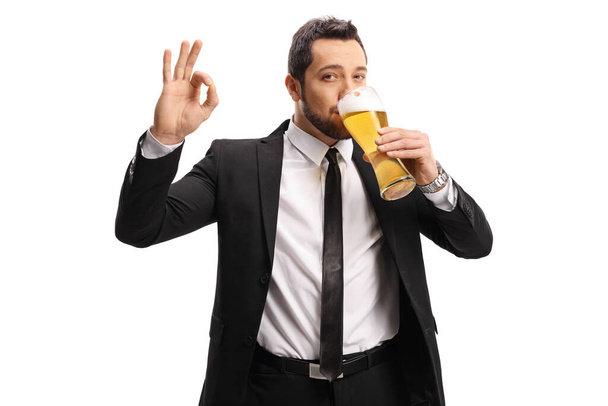 Mies puvussa ja solmio juo lasillisen olutta ja elehtii hieno merkki eristetty valkoisella taustalla
 - Valokuva, kuva