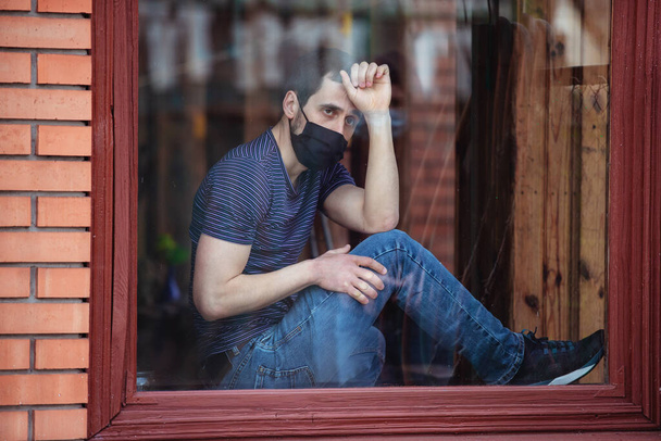 Ein Mann bleibt während der Quarantäne isoliert zu Hause. Coronavirus-Pandemie. Der Typ schaut aus dem Fenster auf die Straße - Foto, Bild