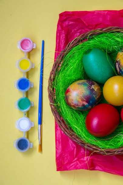 Nido de hierba verde en una cesta con huevos de Pascua de pollo de colores, huevos pintados multicolores y pinturas, tradición de Pascua, concepto de celebración
  - Foto, Imagen