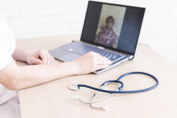 GP ad otthont egy online találkozónak egy idős, karantén alá helyezett beteggel otthon. Női orvos az asztalnál beszél egy idős nővel egy webkamerán, és kezelési ajánlásokat ad. - Fotó, kép