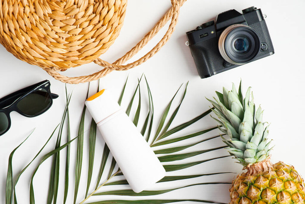 Flat lay traveller accessories on white background with tropical palm leaf. Top view camera, sunglasses, rattan handbag, pineapple, suntan lotion. Summer background. Travel, holiday, vacation concept - Photo, image