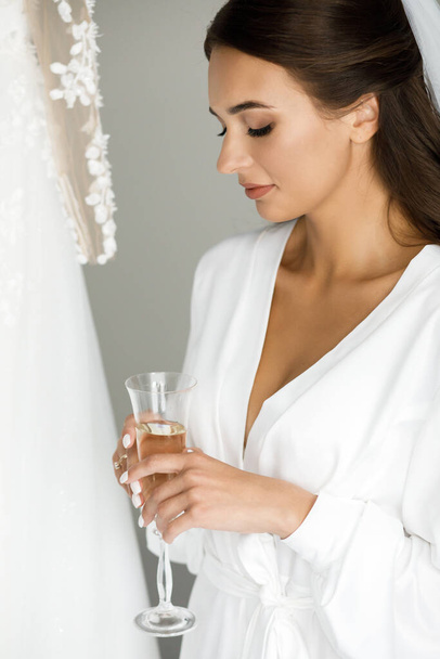 Dziewczyna siedzi na miękkim łóżku, trzymając szklankę z szampanem w rękach. - Zdjęcie, obraz