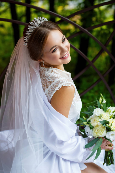 美しい花嫁のベールと白いコートは彼女の手に結婚式の花束と毛布の上に座っている - 写真・画像