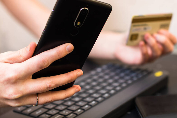Επιλεκτική εστίαση των χεριών που κατέχουν πιστωτική κάρτα και χρησιμοποιώντας smartphone και laptop. Online αγορές, on line έννοια πληρωμής - Φωτογραφία, εικόνα