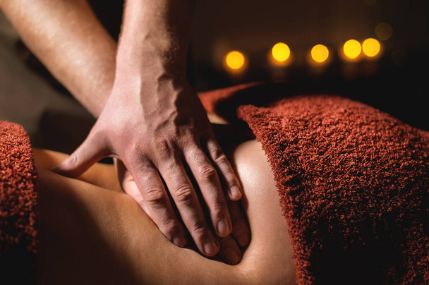 Close-up male hand of a professional physiotherapist masseur doing lumbar massage to a female patient in a massage luxury room with dim light - Zdjęcie, obraz