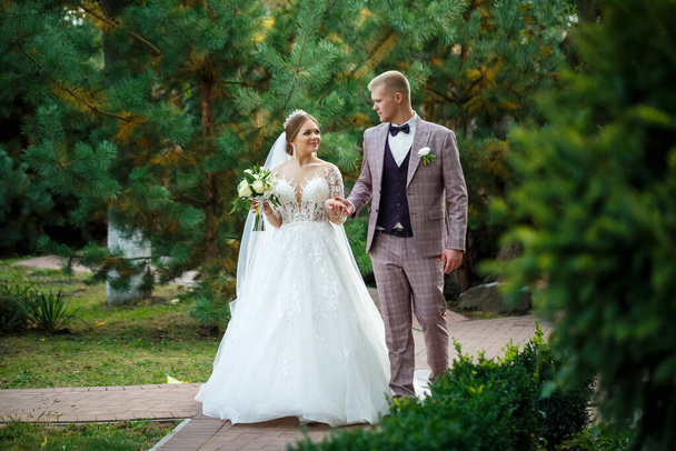 Bride in white dress and groom in costume cuddle and walk in the park - Foto, imagen