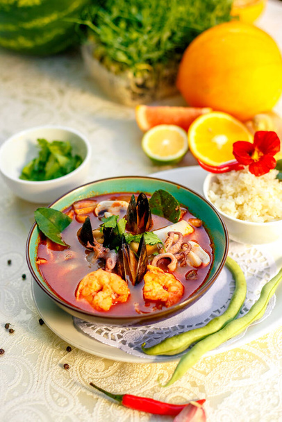 Thai soup tom yam with seafood (octopus, shrimps), herbs and vegetables served on the table with ingredients, healthy food - Photo, Image