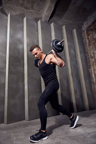 man in black sports uniform with dumbbells on a background of gray wall - Foto, imagen