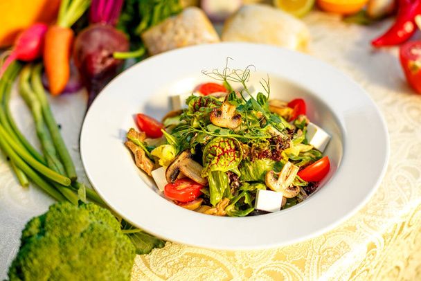 Fresh salad with mushrooms, cheese, tomatoes, herbs and vegetables served on the table with the ingredients, healthy food - Photo, Image
