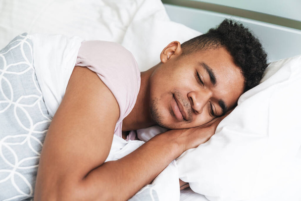 Image of a relaxing sleeping young african guy in the morning in bedroom lies in bed. - 写真・画像