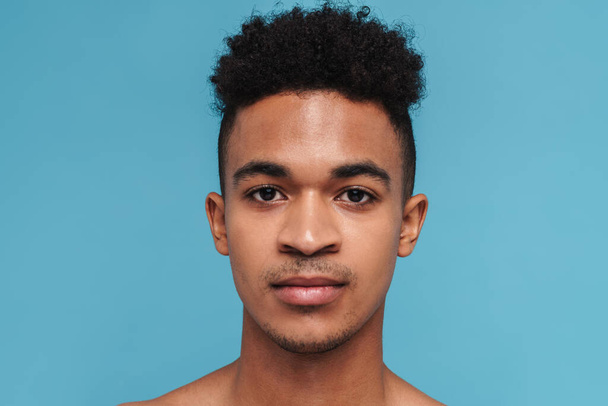 Photo closeup of young african american man posing and looking at camera isolated over blue background - Foto, Imagem