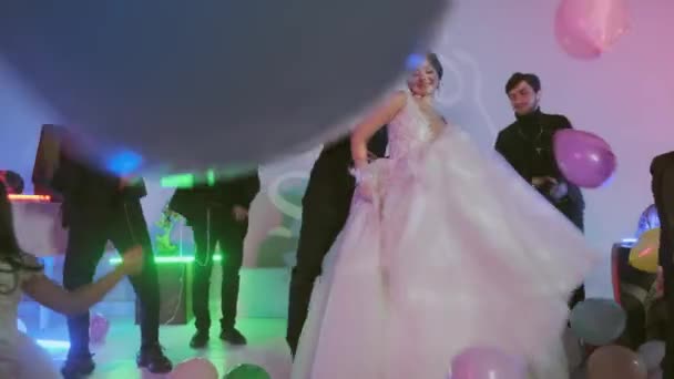Ευτυχισμένος γαμπρός και νύφη χορεύουν με τους επισκέπτες στο γαμήλιο πάρτι, πολύχρωμες μπάλες στο πάτωμα, δωμάτιο με διακοσμημένα με πολύχρωμα φώτα νέον. - Πλάνα, βίντεο