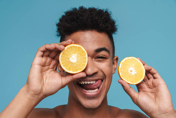 Photo of shirtless african american man making fun with orange isolated over blue background - Zdjęcie, obraz