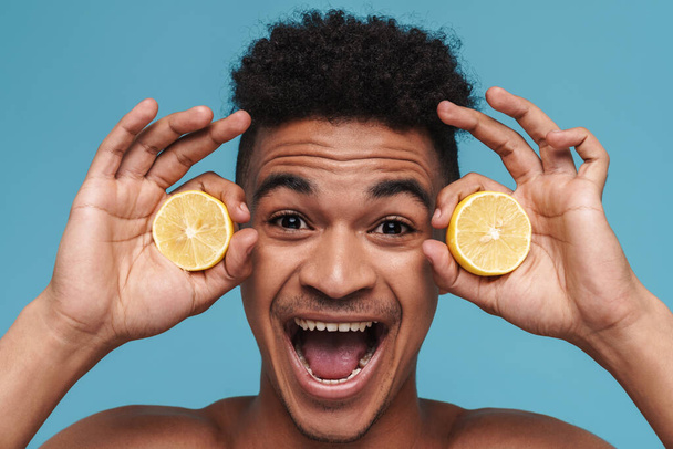 Photo of shirtless african american man making fun with lemon isolated over blue background - Photo, image