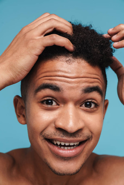 Photo closeup of happy african american man touching her hair and smiling isolated over blue background - Foto, immagini