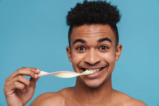 Foto von fröhlichen afrikanisch-amerikanischen Mann lächelnd und Marmelade essen isoliert über blauem Hintergrund - Foto, Bild